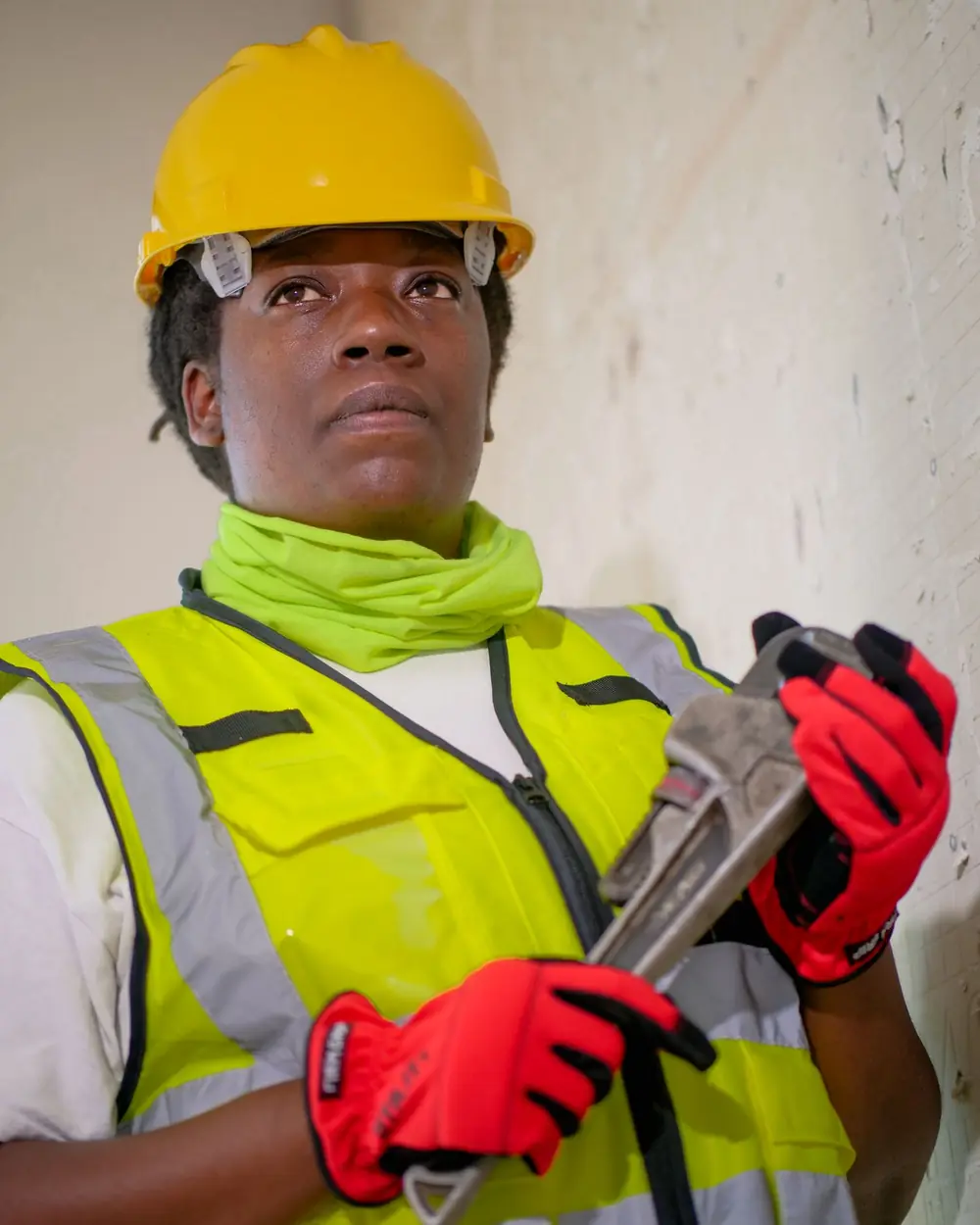 A plumber in a hard hat and hi-vis vest holding a pipe wrench
